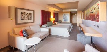 Intérieur des chambres doubles familiales de l'hôtel Lopesan Baobab Resort avec deux lits doubles et un fauteuil.